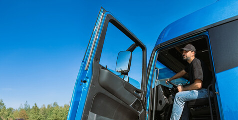 A young man is a professional driver in the cab of a blue truck. Handsome Caucasian guy, a...
