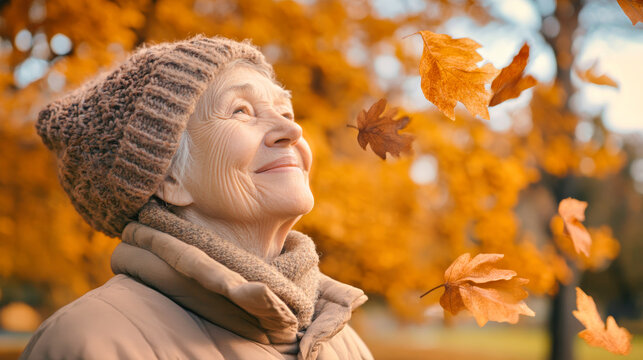 Elderly woman joyfully watches falling leaves in an autumn park, embracing nature's beauty and tranquility during golden hour - Powered by Adobe