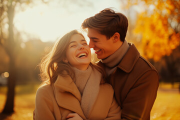 Fototapeta premium A joyful couple shares a laugh while embracing in a sunlit autumn park, surrounded by golden leaves and warm sunlight. 