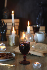 Books, lit candles, red wine, snacks and various deocration on the table. Dark academia or Halloween concept. Selective focus.