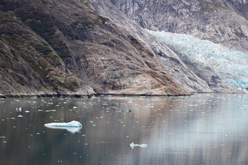 Glacier blue ice view nested in a rocky landscape by the water, showing left side at a mid near distance.