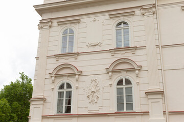 A large, impressive white building featuring a distinctive coat of arms prominently displayed on its facade, surrounded by trees and a blue sky