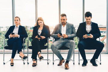 Businesswomen and businessmen using mobile phone while waiting on chairs in office for job interview. Corporate business and human resources concept. uds