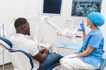 Fototapeta premium Dental hygienist explaining x-ray results to an African male patient during a dental consultation.
