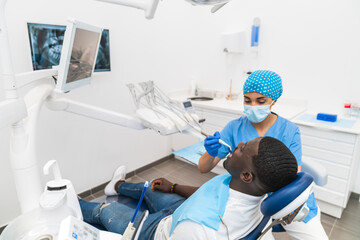 Fototapeta premium Dental hygienist performing a dental cleaning procedure on an African male patient in the clinic.