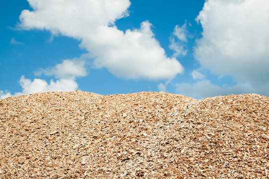 a mountain of wood chips against a background of blue sky and clouds