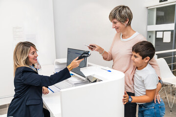 Mother and son interacting with receptionist during payment at a dental clinic reception desk.