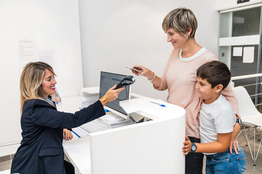 Mother and son interacting with receptionist during payment at a dental clinic reception desk.