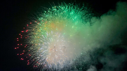 Fototapeta premium A vibrant display of green and red fireworks illuminates the night sky, symbolizing celebration and joy during New Year's Eve