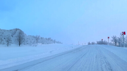 Fototapeta premium A serene, snow-covered rural road under a clear blue sky, representing winter travel challenges and the beauty of remote seasonal landscapes