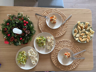 Festive dining table set with an assortment of homemade dishes, complemented by a decorative holiday wreath centerpiece. Warmth and joy of gathering for a shared meal during holiday season