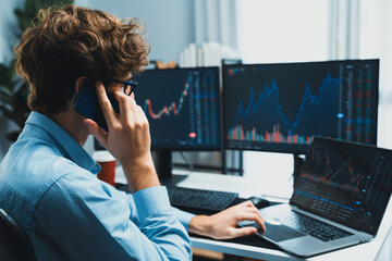 Young investor stock trader discussing on smartphone to broker, looking on dynamic financial exchange investment on screen at back side in current market graph in real time at modern office. Gusher.