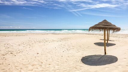 Sunny tropical beach with straw parasols casting shadows on the sand, ideal for summer vacations and relaxation