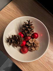 Arrangement of pinecones and red ornaments in a simple white bowl in Christmas, highlighting natural textures and festive colors. Composition captures essence of seasonal decor with a touch of rustic