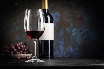 A dark, elegant still life of red wine in a glass with wine bottles and fresh grapes in the background. Perfect for wine-themed compositions
