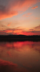 Obraz premium A bright red sunset with intense colors spreading across the sky, reflecting off the surface of a calm lake, creating a mirror-like effect 