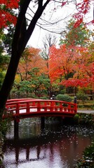 Obraz premium A tranquil red bridge arches over a serene pond surrounded by vibrant autumn foliage