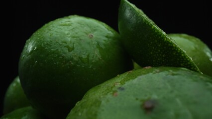 Slices of lime are meticulously arranged in a pile, set against a black background. Each lime slice is captured in stunning detail, its vibrant green hue and enticing texture. Close up. Comestible.