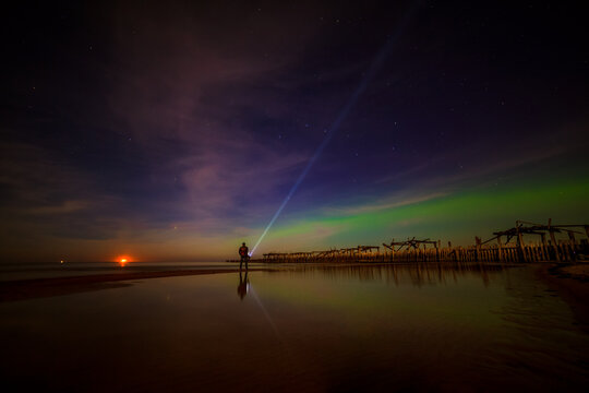 Man with a torch watching northern lights over the Sventoji old pier (Sventosios senasis molas), Sventoji, Palanga, Lithuania