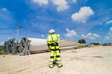 engineers in high visibility safety gear conduct a detailed inspection of a wind turbine blade at a construction site. The massive blade lays on the ground, highlighting renewable energy technology.