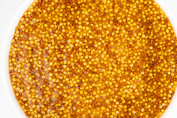Traditional French Dijon mustard in a plate on a white background, top view.