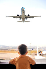 Traveler child. Tourist boy is excitedly waiting for his flight. Kid watching planes taking off from airport window. © Burak