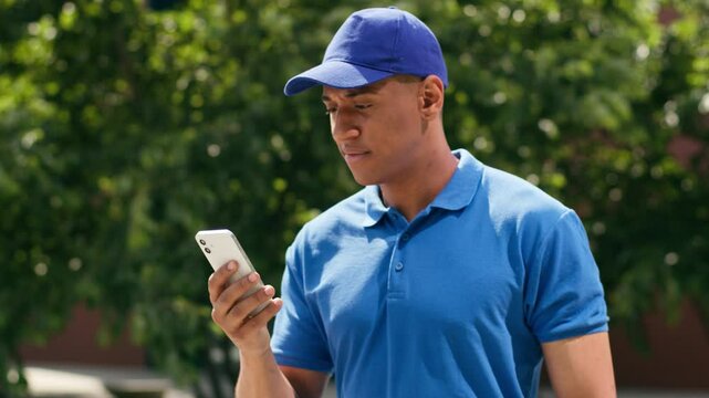 African American courier deliver guy male delivery man service hold order shopping purchase package paper bag walking in city parcel postman looking mobile phone direction navigator searching address