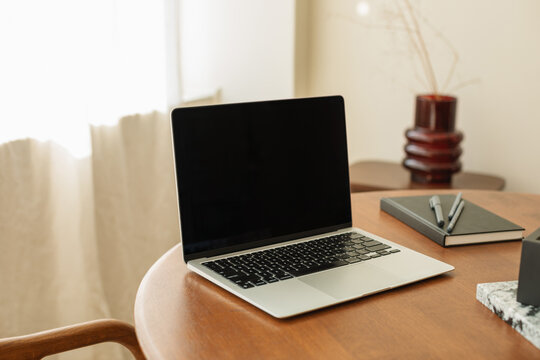Close-up of an open laptop computer with a blank screen on a dining room table with assorted stationery