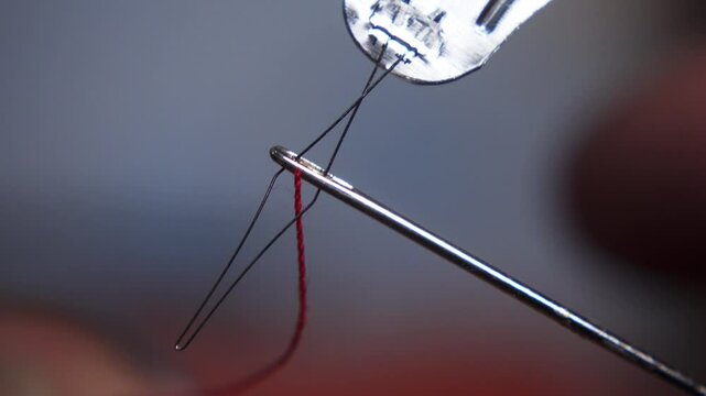 A tailor insert the thread into the eye of the needle with needle threader. macro shot needle threader