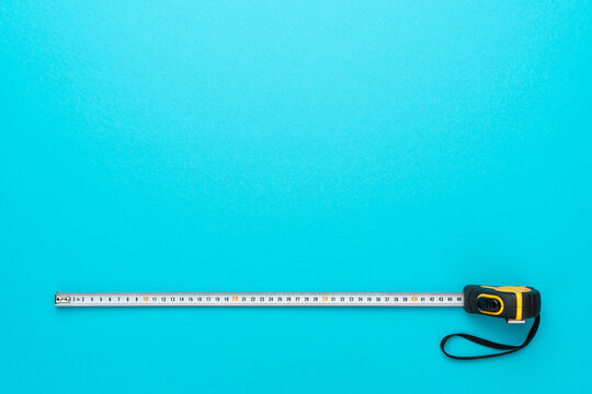 Flat lay image of construction measuring tape. Top view minimalist photo of tape measure on turquoise blue background with copy space.