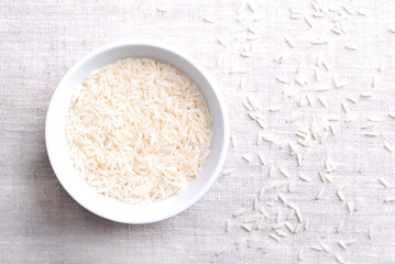 White basmati rice, in a white bowl on linen fabric. Long and slender grains with aromatic smell and taste. Rice grains of an Oryza sativa variety, cultivated in the Indian subcontinent. Photo.