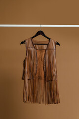 Cowboy-style leather brown vest with fringes hanging on a clothing rack.