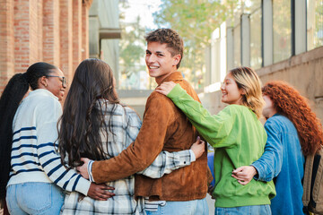 A group of students walk on the university campus, while one of them turns back and looks at the camera smiling. Multiracial teenage friends at the high school going to the class to study together