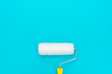 Top view of clean paint roller on the turquoise blue background in the centre of the frame with copy space.