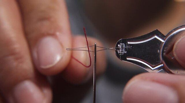 Macro shot of tailor insert the thread through eye of needle with needle threader.