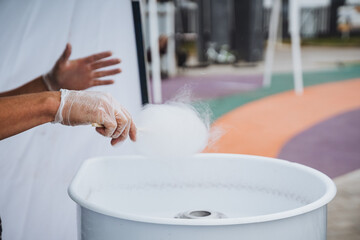 An individual dressed in protective gloves is skillfully preparing cotton candy using a specialized...