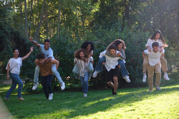 Group of friends is having fun piggybacking in a park on a sunny day