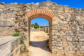 A stone archway with a stone wall on either side. Ruins of the ancient city of Philippi, Greece