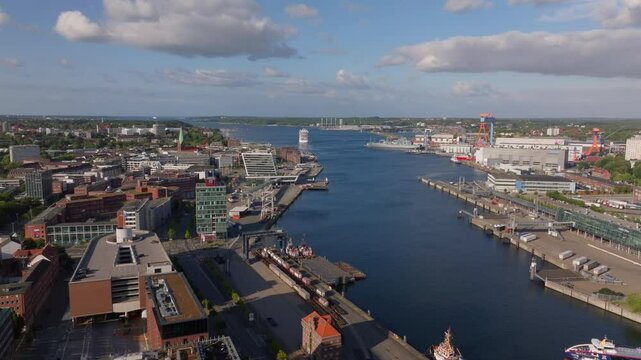 Cruise ship is entering the harbor of Kiel in Germany. The ship is sailing on the Kiel fjord passing industrial buildings and shipyards
