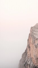 Close-up view of Dolomites peak under a light pink sky during golden hour with soft fog
