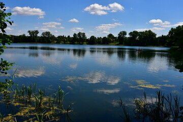A view of a vast river or lake surrounded from all sides with reeds, forests, moors, fields, and pasturelands located next to a small marina or wooden platform and some metal tower seen in Poland