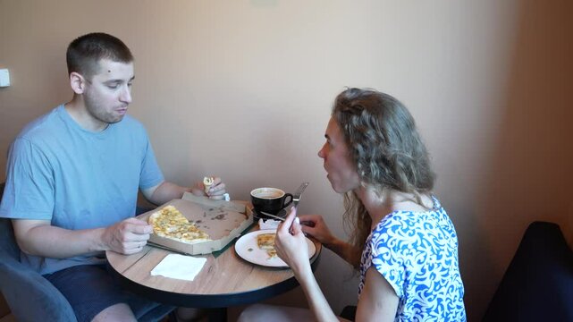 A man and a woman sit at a caf table, enjoying pizza and coffee. The cozy atmosphere and shared meal make for a comfortable and relaxed experience, perfect for socializing and unwinding.