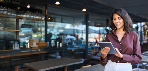 Young adult female entrepreneur owner of coffee shop or bar restaurant using tablet pc application...