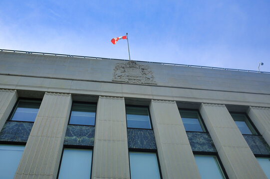 Ottawa, Ontario, Canada. May 20, 2024: The Bank of Canada building in downtown Ottawa, featuring a Canadian flag and the bank's crest.