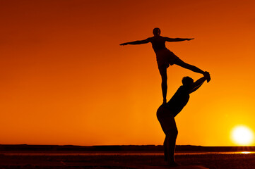 Young adult sports couple doing acro yoga exercises. Silhouette couple practicing yoga at sunset. Slim woman, man do acroyoga. sporty healthy pair doing acrobatic yoga at sunrise. female stand on back