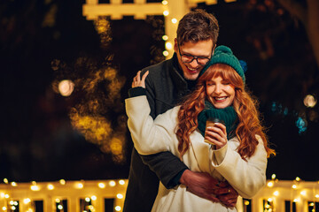 A young affectionate couple is hugging on street on christmas eve.