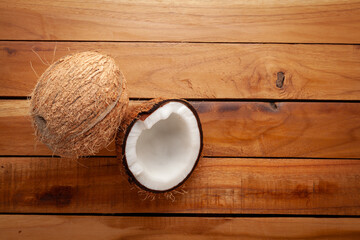 A close-up of a fresh whole coconut and a halved coconut on a wooden surface.