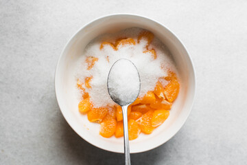 A tablespoon of white sugar, top view of granulated sugar in a silver measuring spoon