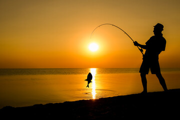 A Happy guy fisherman catching fish by the sea on nature silhouette travel
