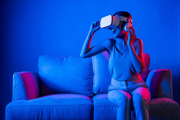 Smart female sitting on sofa wearing VR headset connecting metaverse, future cyberspace community...